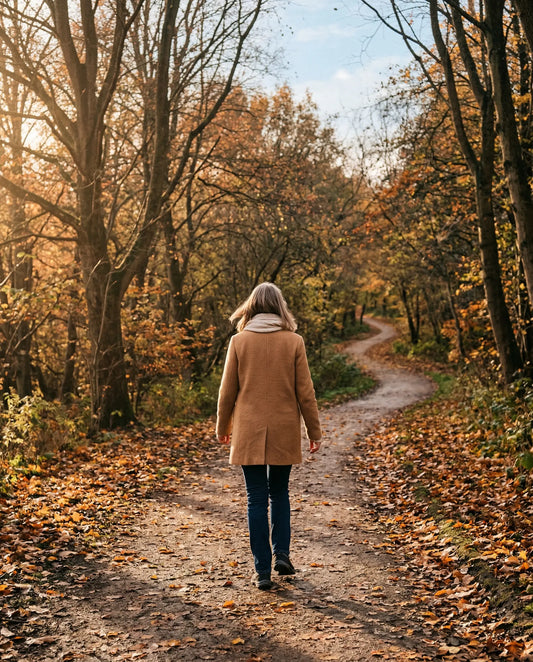 Woman walking alone on an autumn path surrounded by golden leaves